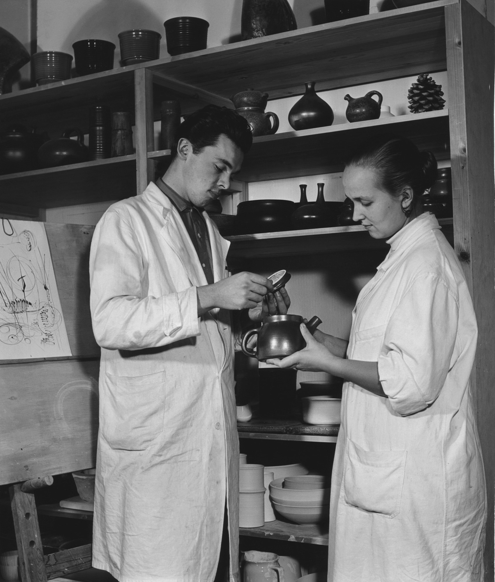 1956年、アラビアの工場で急須を手にするフランチェスカ・マシッティ・リンドと、蓋を持つ夫リカルド・リンド。後ろの棚に壺と水差し
